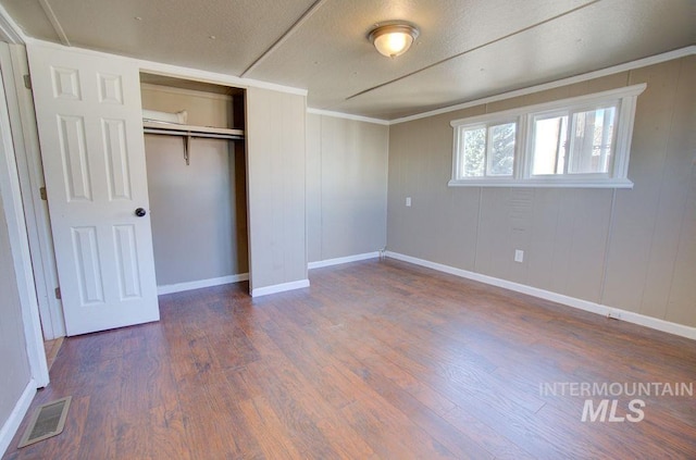 unfurnished bedroom with crown molding, a closet, dark hardwood / wood-style floors, and wooden walls