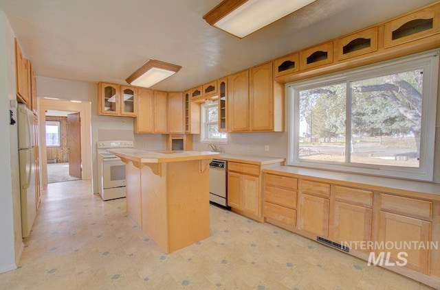 kitchen with a breakfast bar, light brown cabinets, a kitchen island, and white appliances