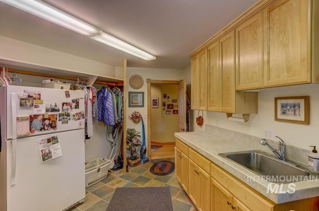 kitchen with light brown cabinetry, tile floors, white fridge, and sink