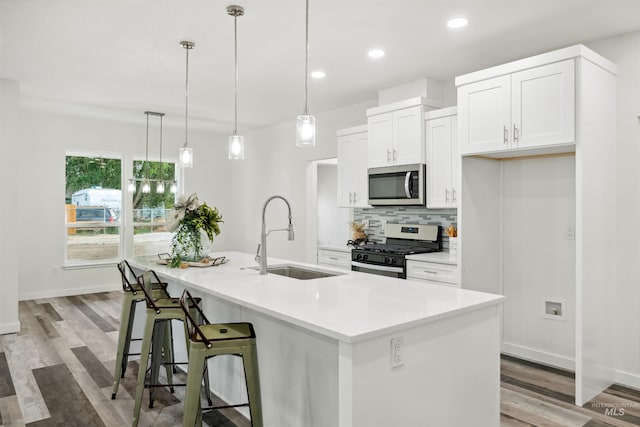 kitchen featuring tasteful backsplash, a sink, white cabinets, stainless steel appliances, and a kitchen island with sink