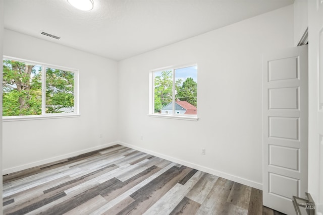 spare room with plenty of natural light, visible vents, and wood finished floors