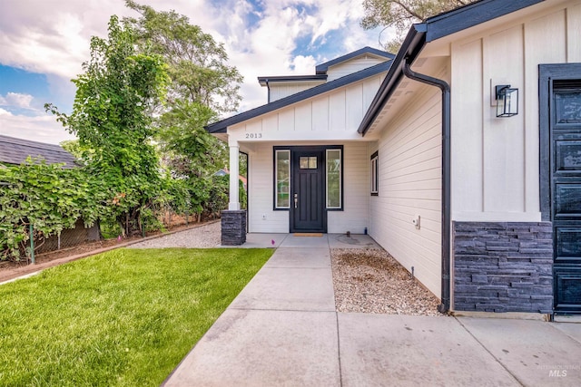 view of exterior entry with a porch, stone siding, a lawn, and board and batten siding