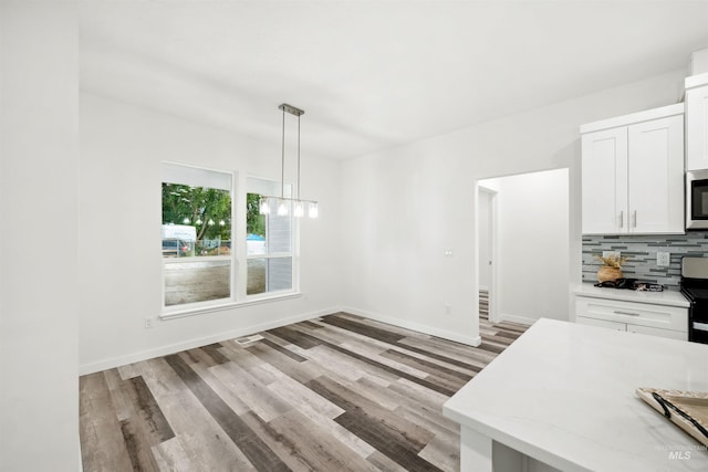 unfurnished dining area with a notable chandelier, light wood-style flooring, and baseboards