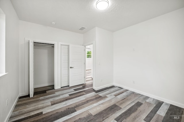 unfurnished bedroom featuring visible vents, wood finished floors, baseboards, and a textured ceiling