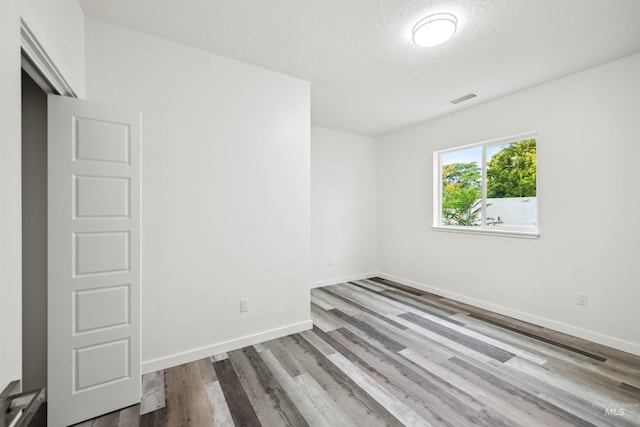 spare room with wood finished floors, visible vents, and baseboards