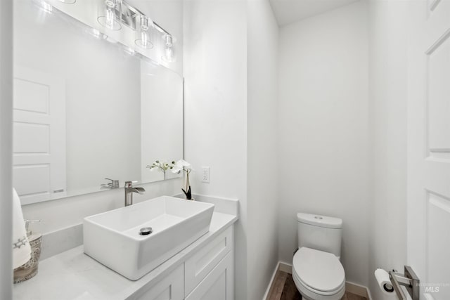 half bathroom with toilet, vanity, and baseboards