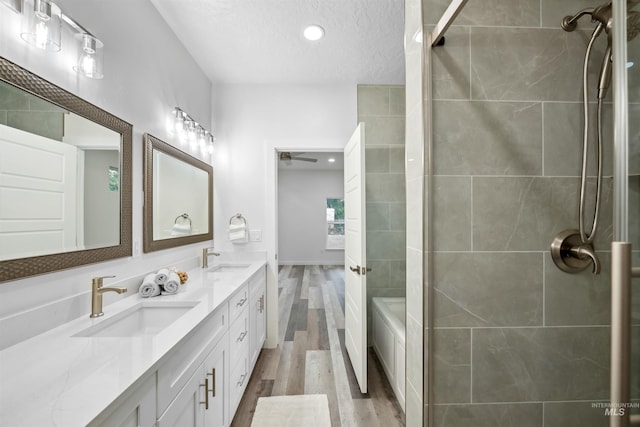 full bathroom with double vanity, wood finished floors, tiled shower, and a sink