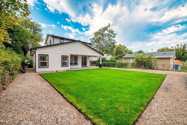 rear view of house featuring a patio, a yard, fence, and board and batten siding