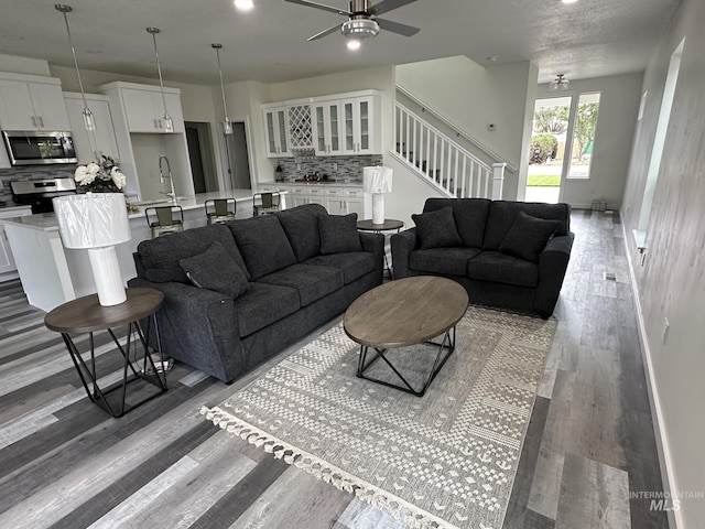 living room featuring stairway, baseboards, ceiling fan, and light wood-style flooring