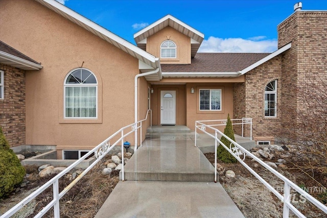 view of exterior entry with stucco siding and roof with shingles