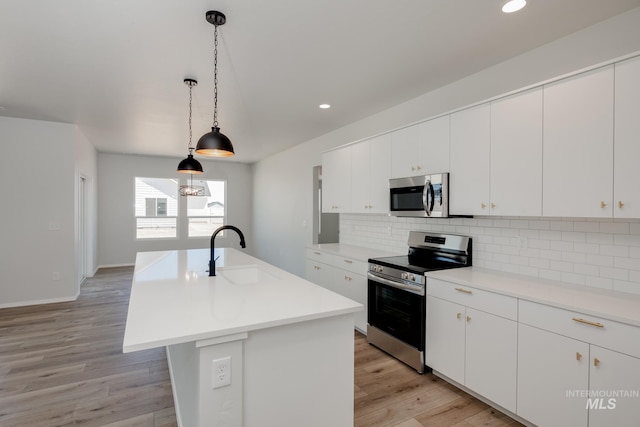 kitchen featuring a kitchen island with sink, sink, light wood-type flooring, and appliances with stainless steel finishes