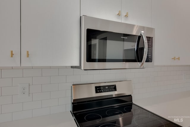 details featuring tasteful backsplash, white cabinets, and appliances with stainless steel finishes