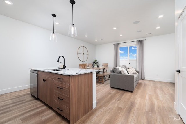 kitchen featuring brown cabinets, open floor plan, hanging light fixtures, a kitchen island with sink, and a sink