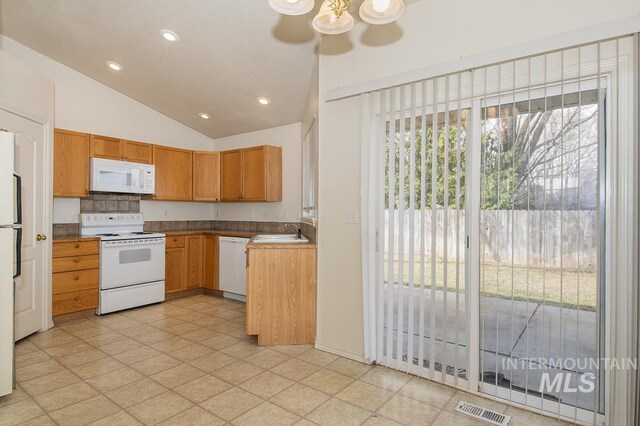 kitchen featuring white appliances, visible vents, a sink, vaulted ceiling, and tasteful backsplash