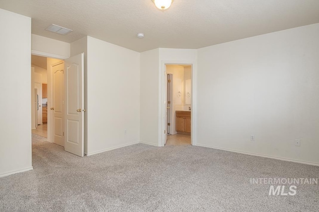 unfurnished bedroom featuring baseboards, light carpet, a textured ceiling, and visible vents