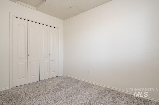 unfurnished bedroom featuring attic access, carpet, a closet, and baseboards