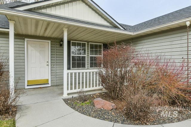 doorway to property with board and batten siding, covered porch, and roof with shingles