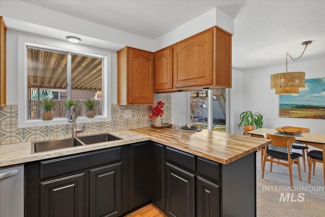 kitchen with a textured ceiling, a peninsula, a sink, backsplash, and dishwasher