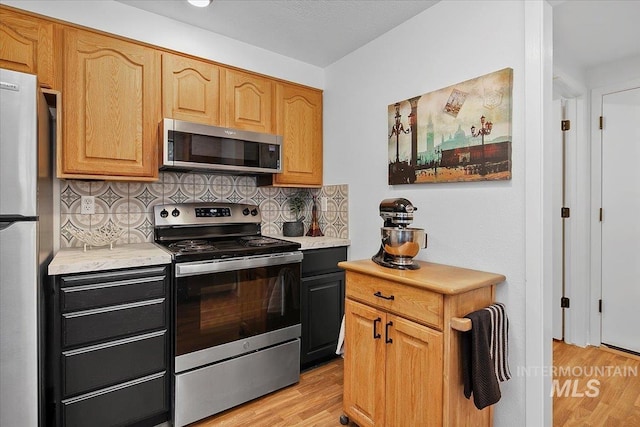 kitchen featuring stainless steel appliances, light wood-type flooring, light countertops, and decorative backsplash