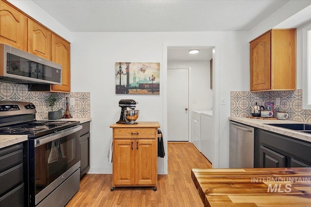 kitchen featuring stainless steel appliances, washer and dryer, light wood-type flooring, and light countertops