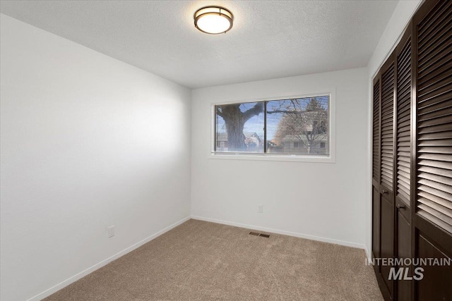 unfurnished bedroom featuring a closet, light colored carpet, visible vents, a textured ceiling, and baseboards