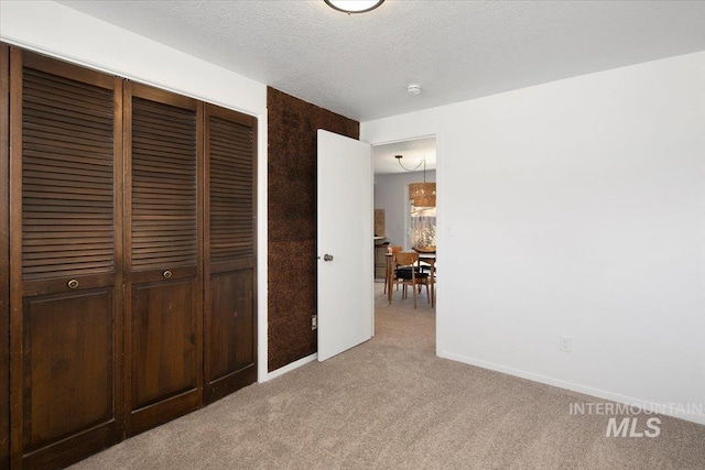 unfurnished bedroom with a textured ceiling, baseboards, a closet, and light colored carpet