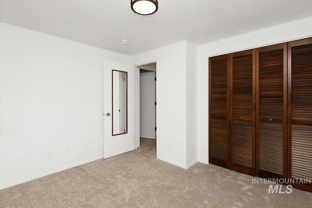 unfurnished bedroom with light carpet, a textured ceiling, baseboards, and a closet