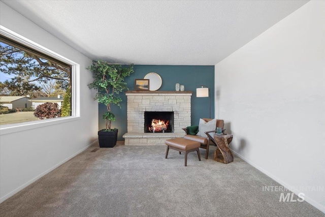 living area with a stone fireplace, carpet flooring, a textured ceiling, and baseboards