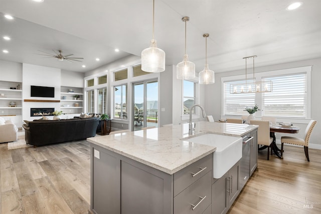 kitchen featuring gray cabinets, a sink, light wood-style floors, a ceiling fan, and a kitchen island with sink