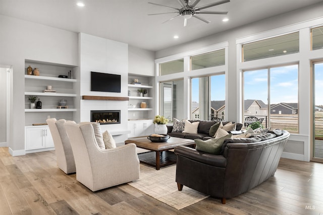 living room with light wood-style flooring, baseboards, a large fireplace, a ceiling fan, and built in features