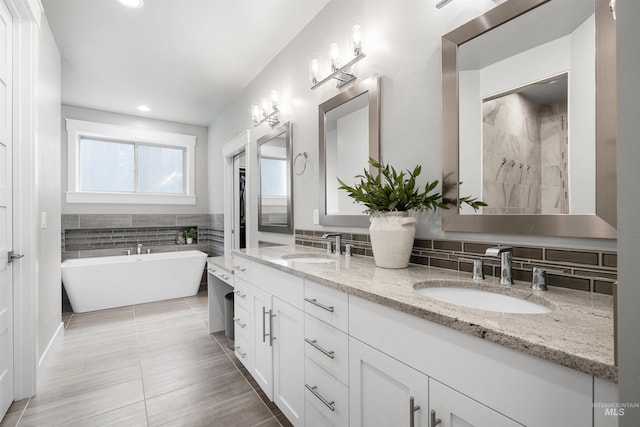 bathroom with double vanity, a sink, tasteful backsplash, and a freestanding bath