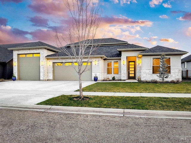 prairie-style home featuring stone siding, a garage, stucco siding, a front lawn, and driveway