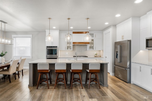 kitchen featuring white cabinets, light wood-style flooring, decorative backsplash, and stainless steel appliances