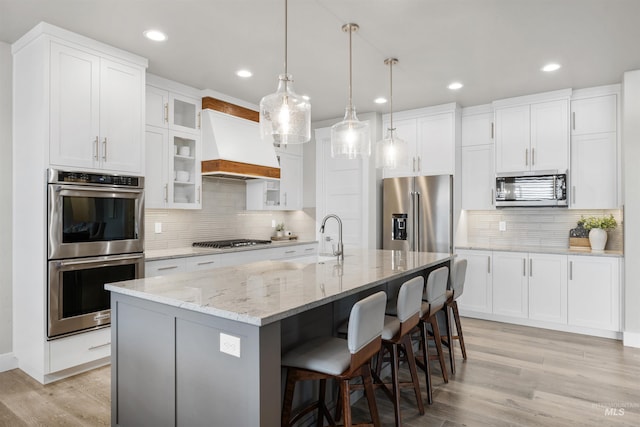 kitchen featuring a breakfast bar area, custom range hood, a sink, light wood-style floors, and appliances with stainless steel finishes