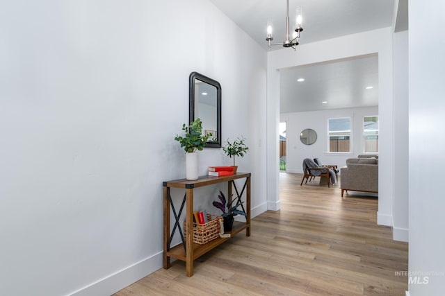 corridor with light wood finished floors, a chandelier, recessed lighting, and baseboards