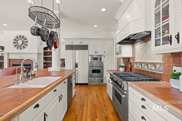 4119 N Park Ln, Eagle, ID 83616 - kitchen featuring built in appliances, tile counters, custom exhaust hood, glass insert cabinets, and white cabinetry