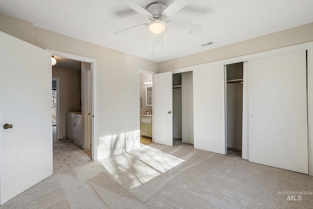 unfurnished bedroom with ensuite bath, ceiling fan, separate washer and dryer, light carpet, and two closets