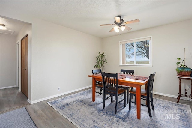 dining room featuring a ceiling fan, visible vents, wood finished floors, and baseboards