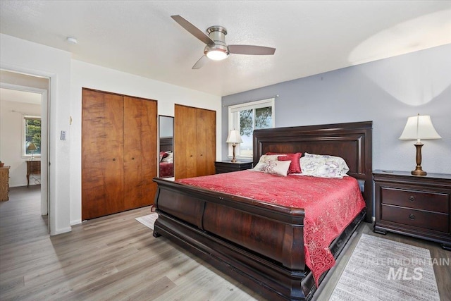 bedroom featuring light wood finished floors, baseboards, two closets, and a ceiling fan