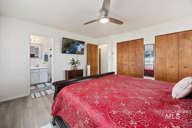bedroom with connected bathroom, two closets, ceiling fan, wood finished floors, and a sink