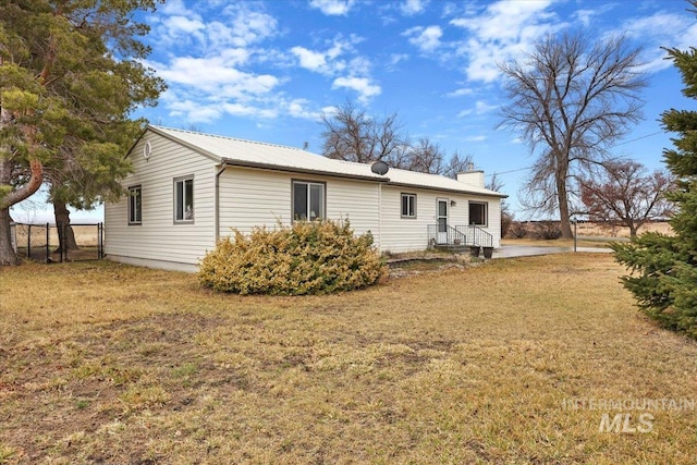 rear view of property featuring a yard, metal roof, a chimney, and fence