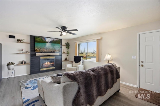 living area featuring baseboards, a large fireplace, ceiling fan, and wood finished floors