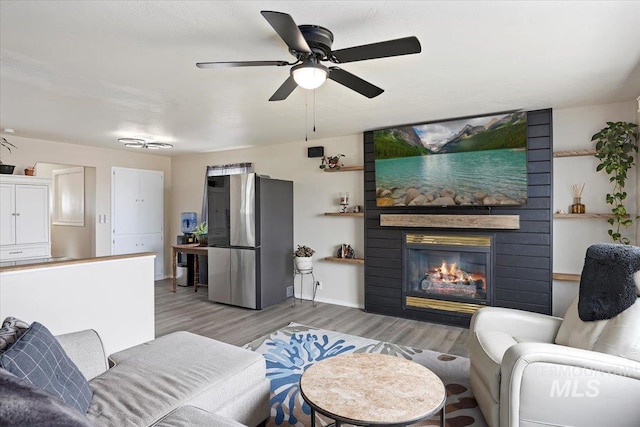 living room featuring a fireplace, a ceiling fan, and light wood-type flooring