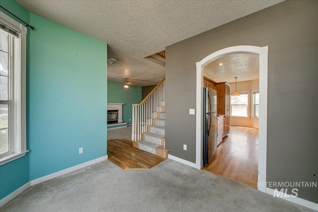 1239 Willow Creek Dr, Nampa, ID 83686 - staircase featuring a textured ceiling, ceiling fan, carpet floors, arched walkways, and a glass covered fireplace