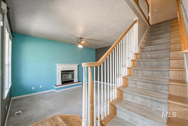 1239 Willow Creek Dr, Nampa, ID 83686 - stairs featuring a ceiling fan, a glass covered fireplace, a textured ceiling, carpet flooring, and baseboards