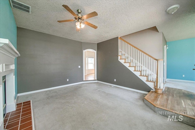 1239 Willow Creek Dr, Nampa, ID 83686 - unfurnished living room featuring a ceiling fan, a textured ceiling, arched walkways, a tiled fireplace, and stairs