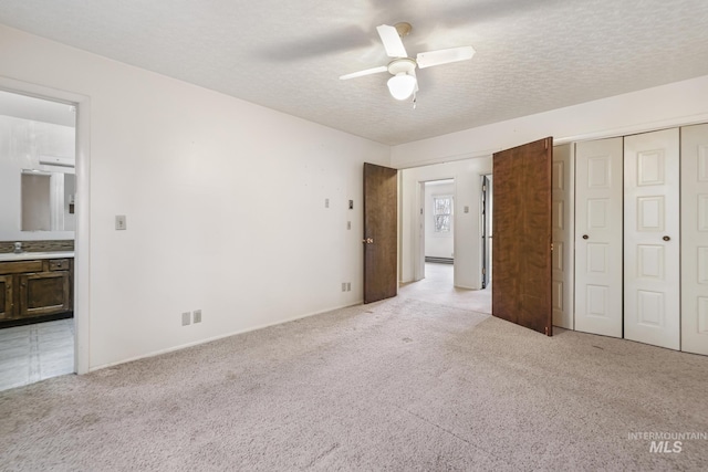 unfurnished bedroom with ensuite bath, ceiling fan, a textured ceiling, light colored carpet, and a closet