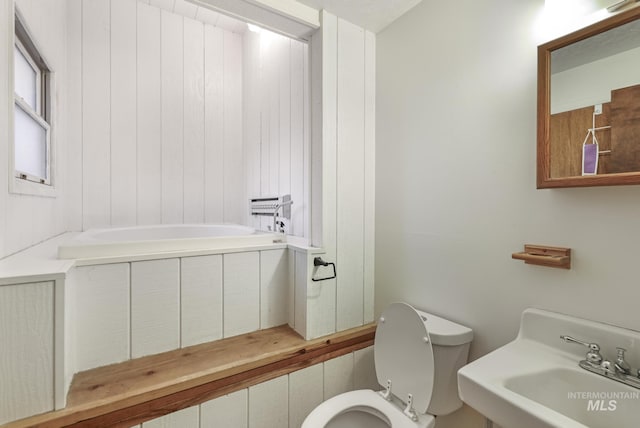 bathroom with a tub to relax in, toilet, and sink