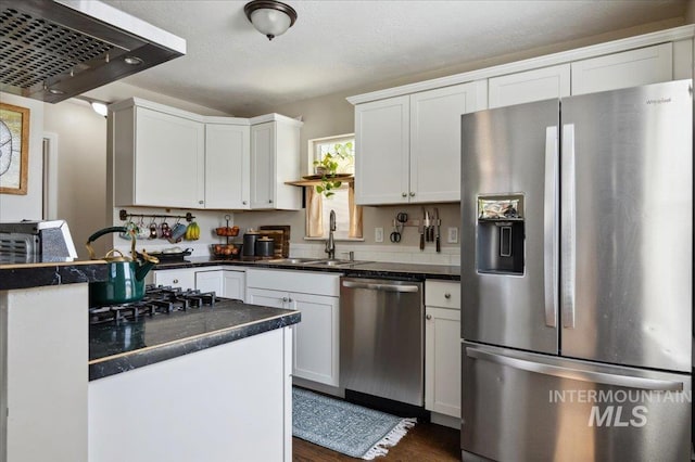 kitchen with white cabinets, dark countertops, a sink, stainless steel appliances, and range hood
