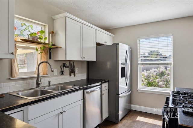 kitchen with dark countertops, baseboards, a sink, dark wood finished floors, and stainless steel appliances